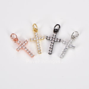 May include: Four small cross charms with clear cubic zirconia stones. The crosses are in gold, rose gold, silver, and black.