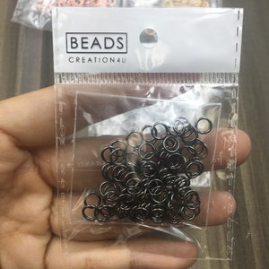 May include: A clear plastic bag filled with black jump rings. The bag has a white label with the text "BEADS CREATION4U".