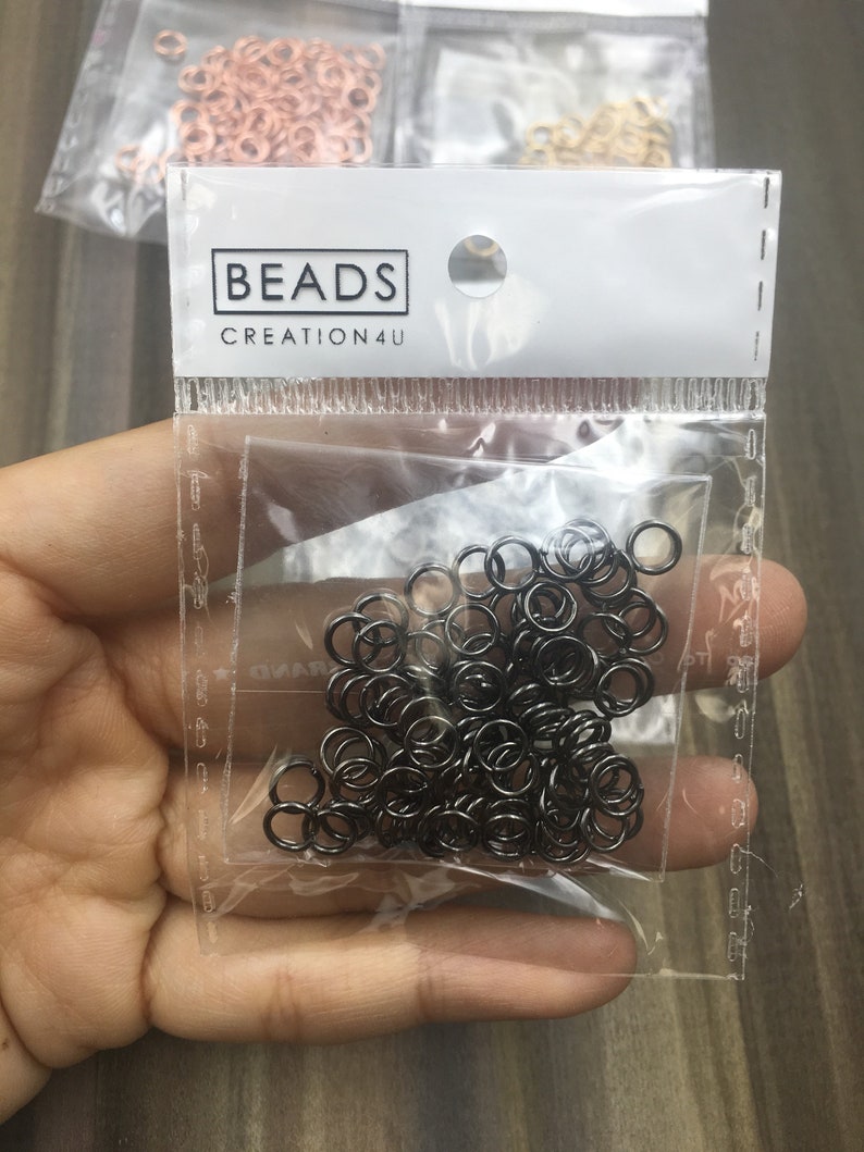 May include: A clear plastic bag filled with black jump rings. The bag has a white label with the text "BEADS CREATION4U".