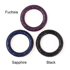 May include: Three circular jewelry pieces in fuchsia, sapphire, and black. Each ring is densely covered with small, sparkling stones. The fuchsia ring is at the top, the sapphire ring is at the bottom left, and the black ring is at the bottom right. The text "Fuchsia", "Sapphire", and "Black" are below each ring.