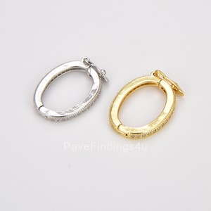 Könnte beinhalten: Zwei ovale Verschlüsse mit einer Pavé-Fassung aus klaren Zirkonia-Steinen. Ein Verschluss ist silberfarben und der andere goldfarben.