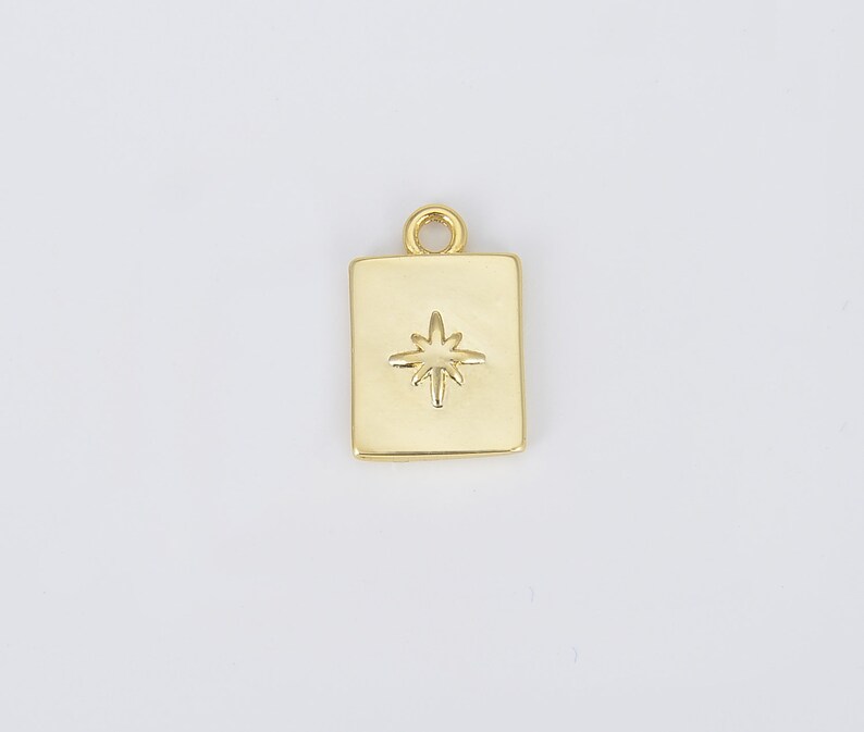May include: Gold charm with a square shape and a star design. The star is raised and has a slightly textured surface.