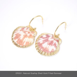May include: A pair of gold-filled earrings featuring natural scallop shells. The shells have a pink and white pattern, and are framed with gold. The earrings have a hoop design. The text at the bottom reads "ER051: Natural Scallop Shell Gold Filled Earwear."