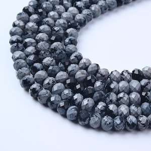 May include: Strands of faceted, round gemstone beads in shades of gray and black. The beads have a speckled pattern and a polished finish, ideal for jewelry making. The beads are strung together, creating a curved shape.