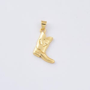 May include: A gold-colored pendant in the shape of a cowboy boot. The boot has a detailed design and a loop at the top for a chain. The pendant is likely made of metal and is displayed against a white background.
