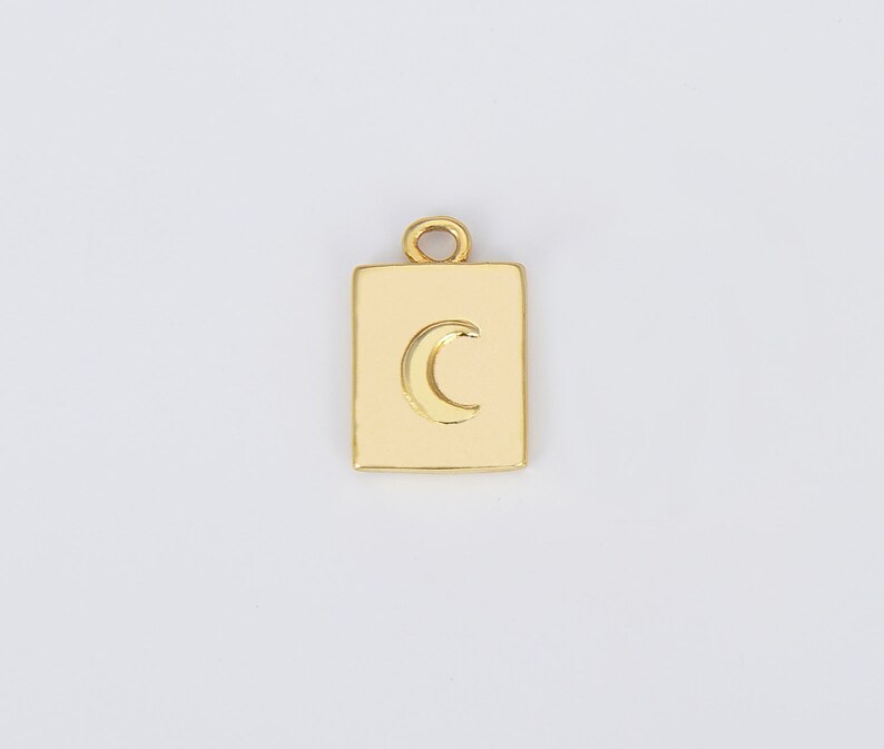 May include: Gold charm with a crescent moon design in a square shape.