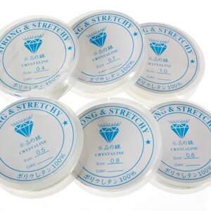 Puede incluir: Seis carretes de hilo el&aacute;stico transparente, cada uno etiquetado con el texto "Strong & Stretchy" y "Crystaline" en japon&eacute;s. Los carretes est&aacute;n etiquetados con diferentes tama&ntilde;os, que van de 0,4 a 1,0.