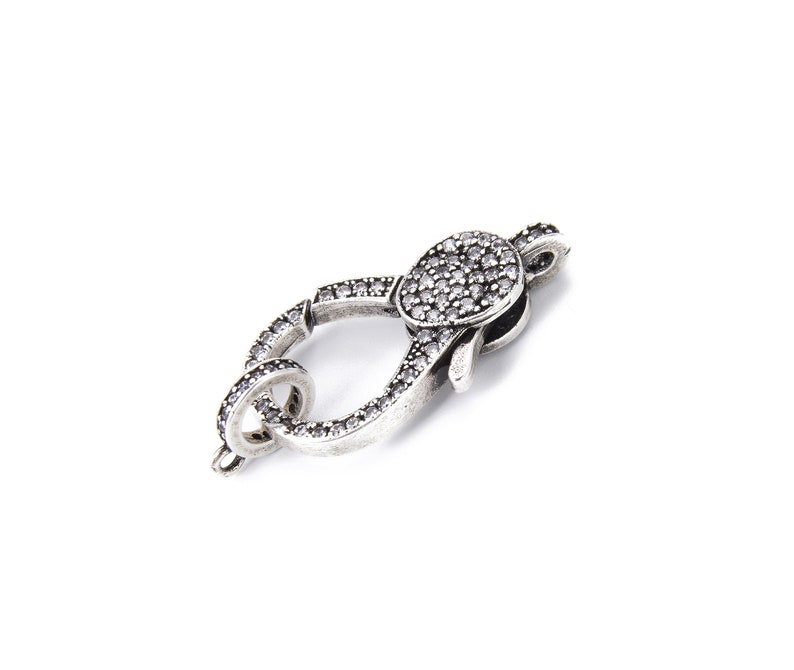May include: Silver-toned clasp with a round, clear crystal-encrusted design. The clasp is designed to be used for jewelry making.