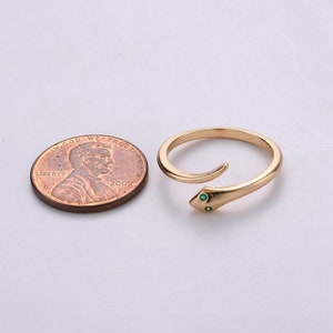 May include: A gold snake ring with two green gemstones for eyes. The ring is shown next to a US penny for size comparison.