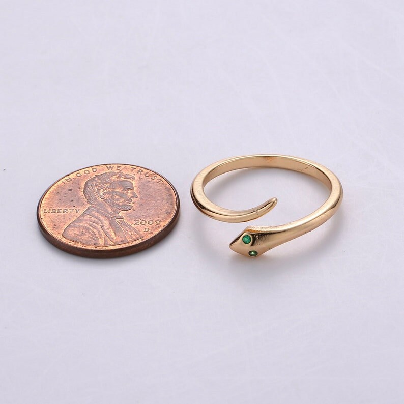 May include: A gold snake ring with two green gemstones for eyes. The ring is shown next to a US penny for size comparison.