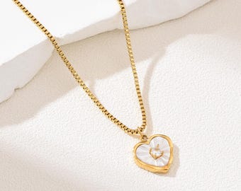 May include: Gold-toned necklace featuring a heart-shaped pendant. The pendant has a white mother-of-pearl inlay and a small, clear gemstone at the center. The chain has a delicate, square link design, and the necklace is displayed on a white surface.