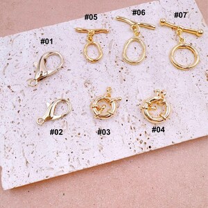 May include: A collection of gold-colored jewelry clasps and connectors. The image displays various styles, including lobster clasps, toggle clasps, and circular connectors. Each piece is numbered for identification, showcasing different designs for jewelry making.