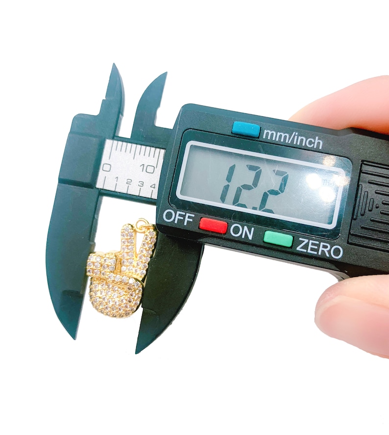 May include: A gold peace sign charm with clear rhinestones is measured with a digital caliper. The caliper reads 12.2 mm.