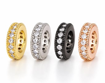 May include: Four circular spacer beads arranged in a row, each featuring a central band of clear, round-cut stones bordered by beaded metal edges. The beads are finished in gold, silver, black, and rose gold tones respectively.