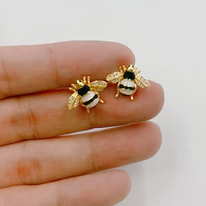 Peut inclure: Une paire de boucles d'oreilles en forme d'abeille dorées avec émail noir et blanc et strass transparents.