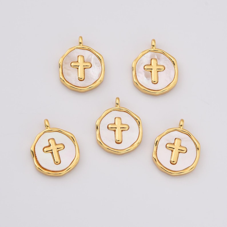 Op de afbeelding: Vijf gouden kruisbedels met witte parelmoer inleg. Elke bedel heeft een lus om aan een ketting of armband te bevestigen.