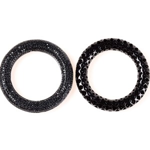 May include: Two black bangles. One is covered in small, sparkling black stones. The other has a geometric, openwork design. Both are circular and sit against a white background.