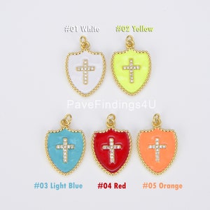 May include: Five gold-tone shield charms with a cross design. Each charm has a different colored enamel: white, yellow, light blue, red, and orange. The crosses are embellished with clear rhinestones.