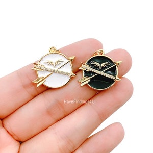 May include: Two gold-tone pendant charms with a circular design. One charm has a white background with black accents and the other has a black background with white accents. Both charms feature a stylised arrow design with a small diamond-like accent.