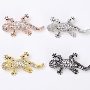 May include: Four jeweled gecko lizard charms in rose gold, gold, silver, and black.