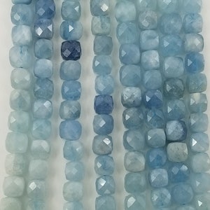 May include: Strands of aquamarine gemstone beads in varying shades of blue. The beads are square-cut with faceted surfaces, creating a sparkling effect. The color palette ranges from pale to deep blue.