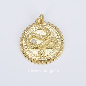 以下が含まれることがあります： 中央に透明なラインストーンをあしらった蛇のデザインの金色のペンダント。ペンダントは小さなビーズの円に囲まれています。