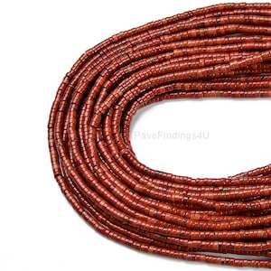May include: A strand of red carnelian beads, each bead is a tube shape with a smooth, polished finish. The beads are arranged in a circular pattern, creating a visual effect of a necklace.
