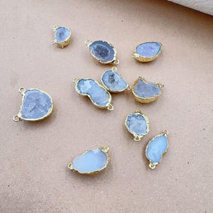 May include: Assortment of ten gold-plated agate gemstone pendants with a white and light purple color. The pendants are in various shapes and sizes, and each has a hole for attaching a chain or cord.