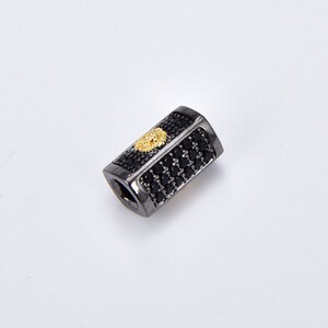 May include: Black and gold rectangular bead with a lion head design. The bead is covered in small black stones.