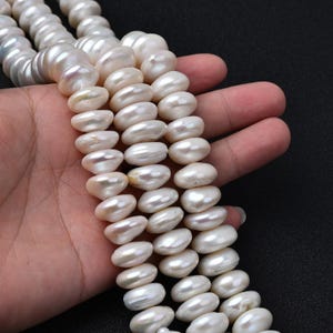 May include: Strands of white, oval-shaped pearls. The pearls have a lustrous sheen and vary slightly in size. The image shows multiple strands, suggesting they are ready for jewelry making or display. The background is a solid black.