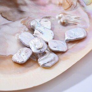 May include: A collection of white baroque pearls in various shapes and sizes, displayed on a shell. The pearls have an iridescent sheen and are arranged in a cluster.