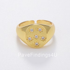 May include: Gold signet ring with a round, oval-shaped top featuring a design of seven small, clear, star-shaped stones.