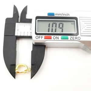 以下が含まれることがあります： デジタルノギスを使用して測定した、金色の金属製留め具は、長さが10.9mmです。留め具は、チェーンやコードを取り付けるために使用される一般的なジュエリーパーツです。