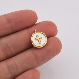 Op de afbeelding: Gouden hanger met een wit emaille kruisontwerp. De hanger is rond en heeft een licht getextureerde rand.