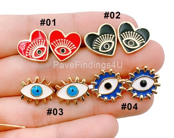 May include: Four pairs of earrings with different designs. The first pair is red heart-shaped earrings with a black eye design. The second pair is black heart-shaped earrings with a black eye design. The third pair is white oval-shaped earrings with a blue eye design. The fourth pair is white oval-shaped earrings with a blue eye design and a gold rim.