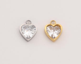 Puede incluir: Dos colgantes en forma de corazón. Uno es plateado, el otro dorado. Ambos tienen un centro de piedra transparente y facetada. Cada colgante tiene un pequeño lazo en la parte superior para sujetarlo a una cadena u otro componente de joyería. Los colgantes se muestran sobre un fondo blanco.