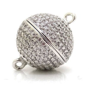 May include: Silver tone magnetic clasp with a round ball design. The ball is covered in small, clear rhinestones.