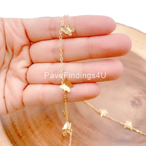 May include: A gold chain necklace with small butterfly charms. The necklace is on a hand, and the background is a wooden surface.