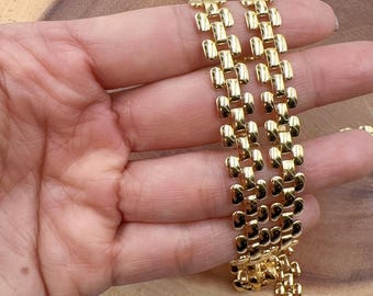 May include: Gold metal chain with a square link design. The chain is shown in a hand, with the links running vertically.