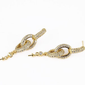 May include: Gold tone earrings with a linked chain design, encrusted with clear cubic zirconia stones.