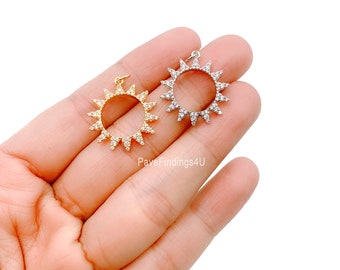 Può includere: Due ciondoli a forma di sole, uno dorato e uno argentato, ciascuno con un anello di cristalli scintillanti e un piccolo anello per appenderli. I ciondoli sono esposti su uno sfondo chiaro.