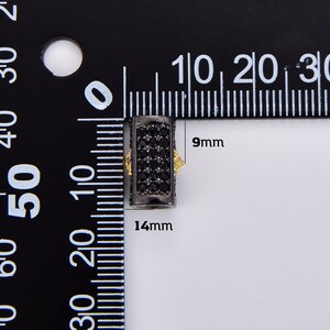 May include: Black and gold-toned metal bead with black cubic zirconia stones. The bead measures 14 mm long and 9 mm wide.