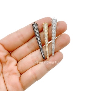 May include: Three cone-shaped pendants with a pave setting of clear cubic zirconia stones. The pendants are in black, gold, and silver.