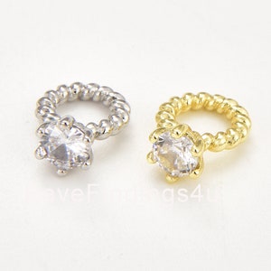 May include: Two ring charms, one silver and one gold, each with a clear, faceted gemstone. The ring bands have a twisted rope design. Ideal for jewellery making or craft projects.