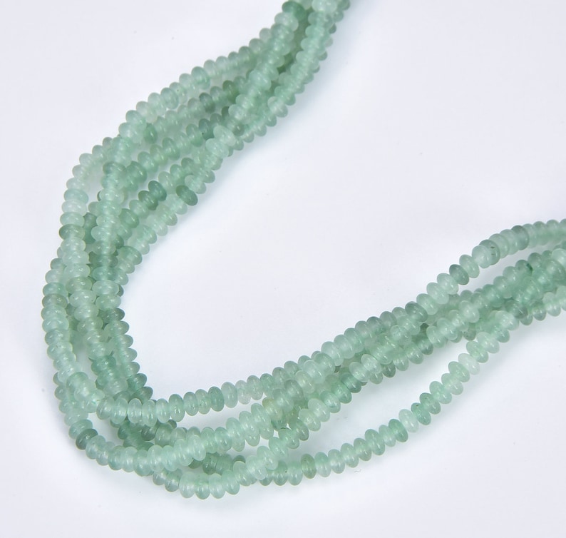 May include: A strand of light green beads, made of natural stone, with a smooth, rounded shape. The beads are strung together on a clear thread.