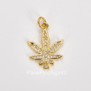 Puede incluir: Encanto de hoja de marihuana de tono dorado con piedras de circonita cúbica transparentes. El encanto tiene un bucle en la parte superior para sujetarlo a un collar o pulsera.