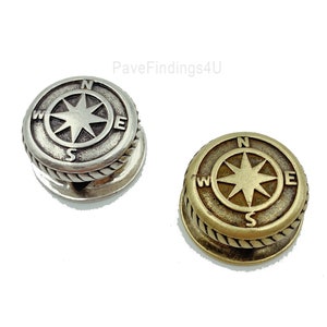May include: Two compass-shaped metal buttons with a rope-like border. The button on the left is silver and the button on the right is gold.