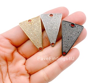 May include: Three triangular pendants in gold, silver, and black, each encrusted with small, sparkling stones. The pendants have a loop at the top and bottom for attaching to jewelry. The pendants are held in a hand.