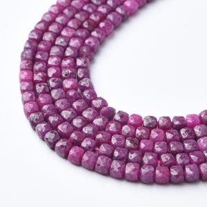May include: Close-up of strands of faceted, deep magenta ruby beads. The beads are square-shaped and strung together, creating a textured and colorful display. The beads are a rich, saturated color.