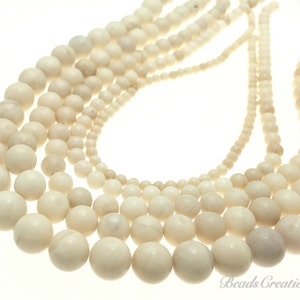 May include: A collection of white round beads of varying sizes, strung together in a necklace style. The beads have a smooth, slightly textured surface.